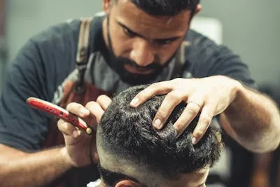 Coiffeur professionnel en train de couper les cheveux dans son salon