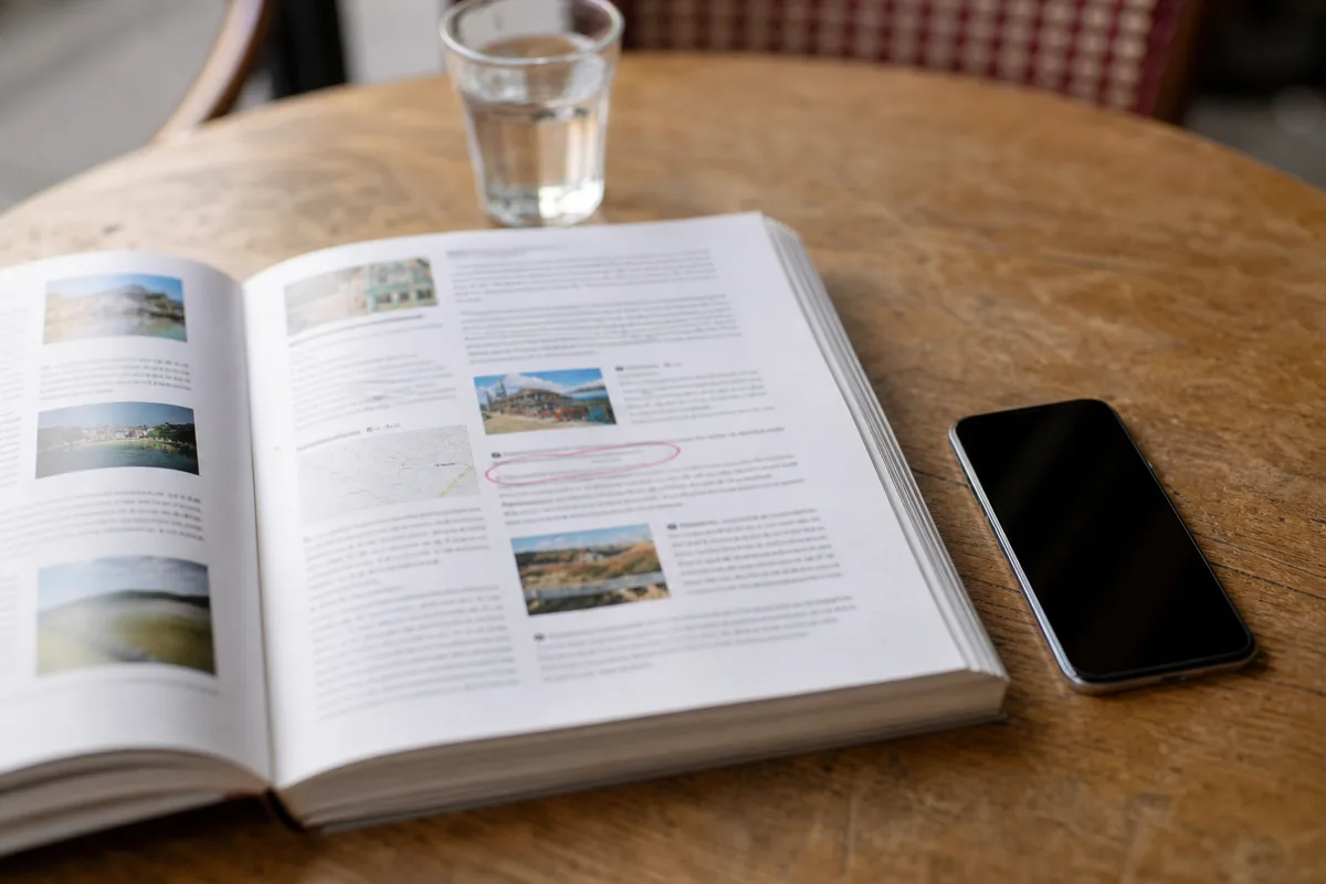 Un guide de voyage ouvert où une adresse est entourée au crayon, un téléphone posé à côté