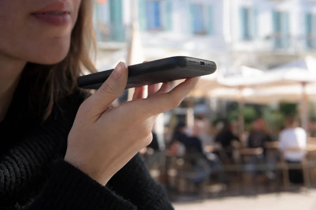 Une main tient un téléphone près de la bouche pour poser une question à voix haute